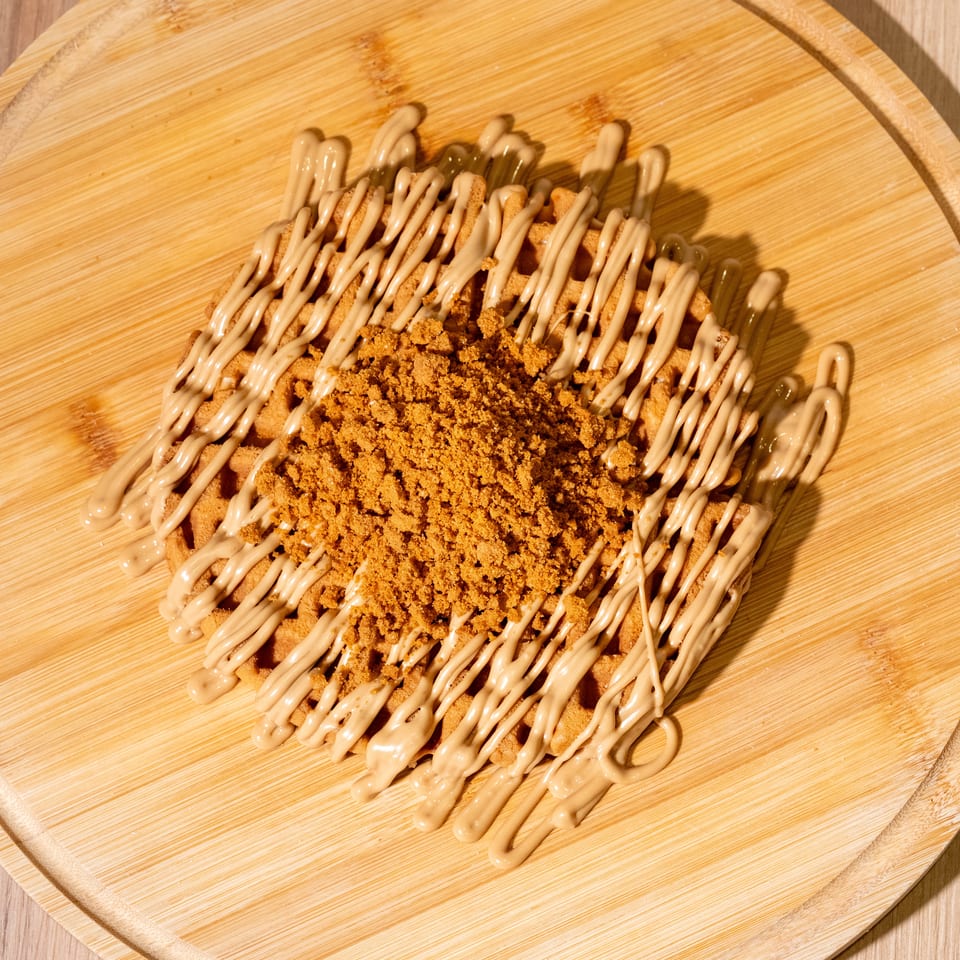 Crispy fried dessert drizzled with creamy sauce and topped with golden cookie crumbs on a round wooden serving board.