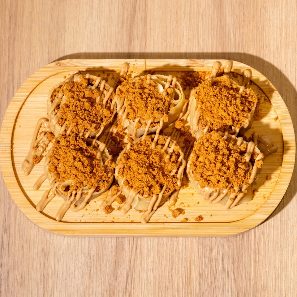 Six dumplings topped with crispy crumbs and drizzled sauce on a wooden serving platter.